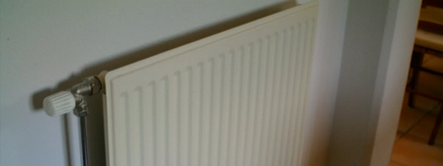 Radiator panou alb montat pe perete, fotografiat din lateral, cu robinet și grilă superioară vizibile