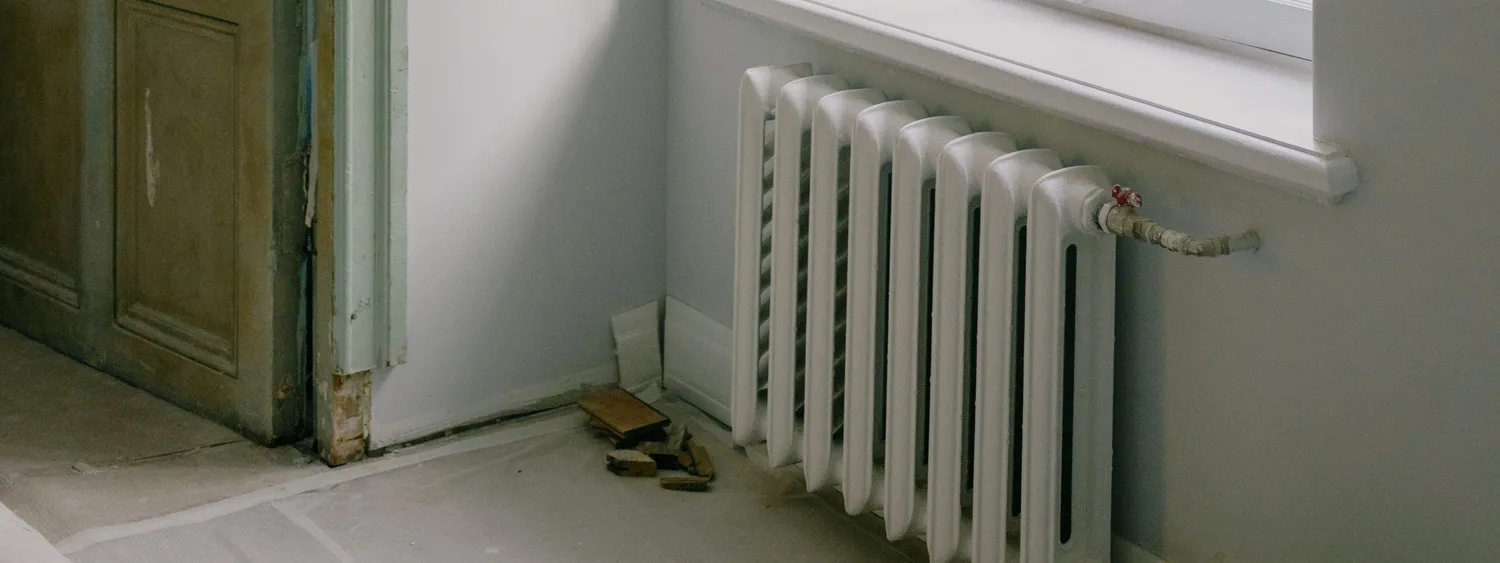 Radiator vechi cu elemenți albi, montat sub fereastră într-o încăpere în renovare