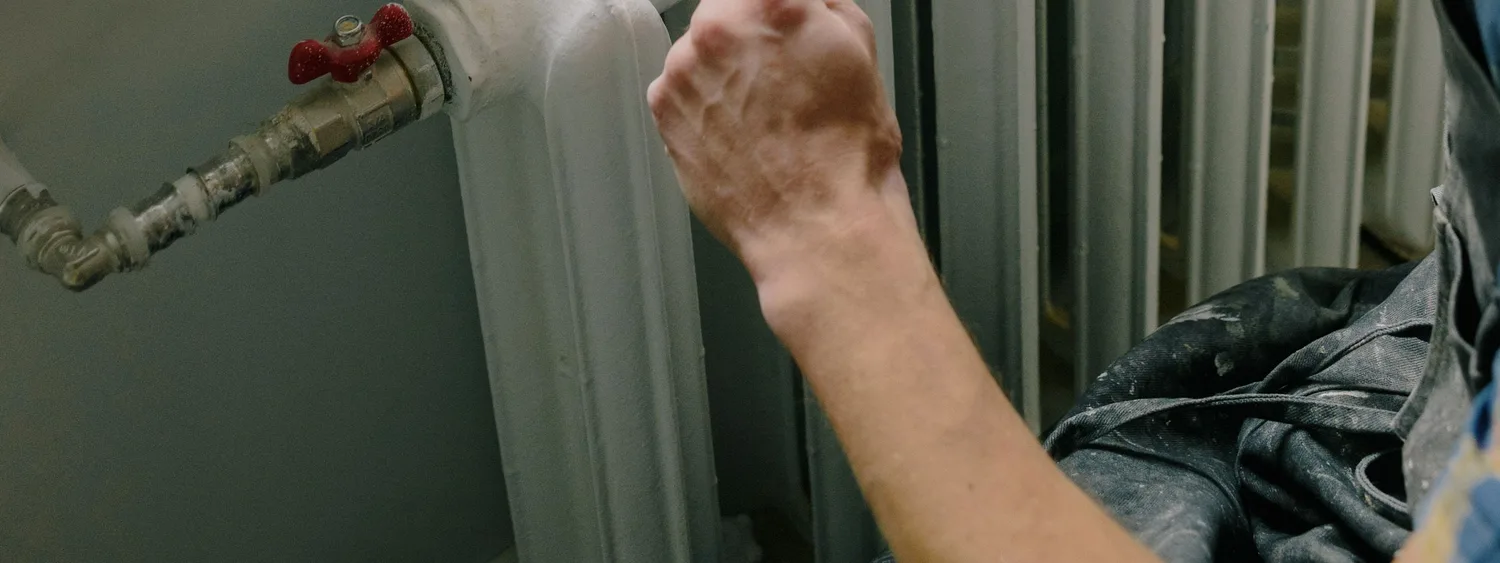 Persoană care măsoară un radiator vechi lângă fereastră